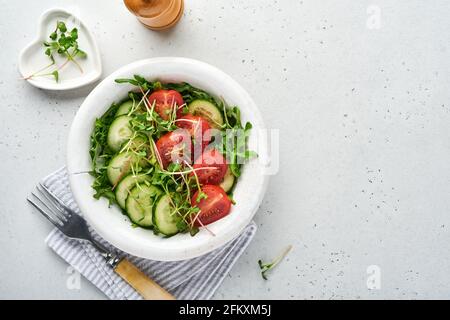 Frischer Salat mit Tomaten, Gurken, Gemüse, mikrogrünen Radieschen auf weißem Teller auf grauem Steingrund. Blick von oben. Konzept vegan und gesund Stockfoto