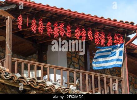 Chilischoten trocknen und eine griechische Flagge fliegen, auf dem Balkon eines Hauses im Fischerdorf Psarades am Prespa-See, Mazedonien, Nord-Greec Stockfoto