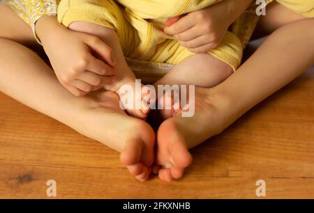Zwei Schwestern sitzen auf dem Holzboden, zwei kleine Mädchen mit den Füßen Stockfoto