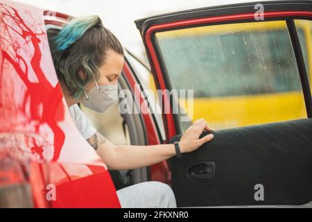 Spanische Frau, die mit der Maske aus dem aussteigen Rückseite eines roten Autos Stockfoto