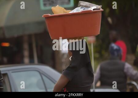 Afrikanische Frau mit einem Ohrring, die in der Stadt Yaounde, Kamerun, einen Plastikkorb auf dem Kopf trägt Stockfoto