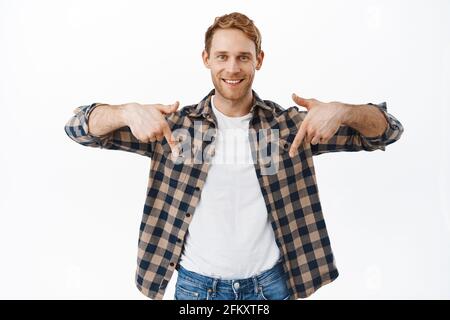 Ihre Anzeige unten. Lächelnder, hübscher Rotkopfmann, der mit den Fingern auf das Logo-Banner zeigt und auf weißem Hintergrund den Promo-Text zeigt Stockfoto