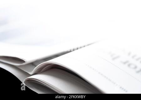 Offene gefaltete Zeitung mit unlesbarer Überschrift liegt schräg auf einem schwarzen Tisch. Fotografiert aus einem niedrigen Blickwinkel, sehr geringe Schärfentiefe Stockfoto