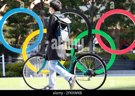 Tokio, Japan. Mai 2021. Ein Mann mit Gesichtsmaske geht auf dem Fahrrad an den Olympischen Ringen in der Nähe des Nationalstadions in Tokio vorbei. Kredit: SOPA Images Limited/Alamy Live Nachrichten Stockfoto