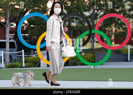Tokio, Japan. März 2021. Eine Frau mit Gesichtsmaske geht mit ihrem Haustier an den Olympischen Ringen in der Nähe des Nationalstadions in Tokio vorbei. Kredit: James MATSUMoto/SOPA Images/ZUMA Wire/Alamy Live Nachrichten Stockfoto