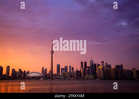 Die Skyline von Toronto mit orangefarbenem Leuchten am Himmel bei Sonnenuntergang, von der Toronto Island aus gesehen. Stockfoto