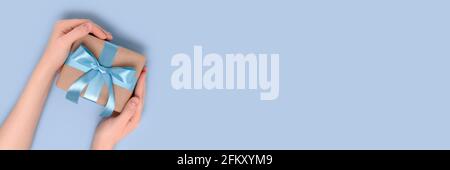 Banner mit weiblichen Händen halten Geschenkbox auf blauem Hintergrund. Geschenk gebunden mit einem Band. Stockfoto