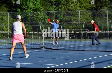 Zwei ältere Männer treten in einem Wettkampfspiel von Pickle Ball gegen eine Frau an. Sie spielen auf einem Tennisplatz. Stockfoto