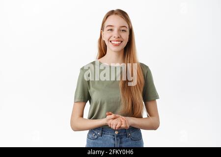 Bereit, Kunden zu helfen und Fragen zu beantworten. Lächelnde, freundliche junge Frau, die die Hände auf der Brust zusammenhält, die Kamera anschaut, Assistentin hilft Stockfoto