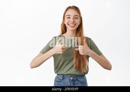 Ja, Sehr gut. Lächelndes hübsches Mädchen zeigt Daumen nach oben, sieht zufrieden aus und nickt in Zustimmung, geben ihr Unterstützung, empfehlen Produkt, Lob Stockfoto