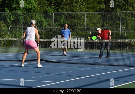 Senioren spielen eine Partie von Doppelgängeln in Pickle Ball. Zwei Männer sind in einem Team. Rüde im roten Hemd schwingt, um auf einen luftgetragenen, gelben Pickle-Ball zu treffen. Stockfoto