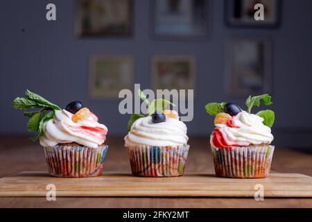 Drei Cupcakes in Cremefarben auf einem Holzbrett Stockfoto