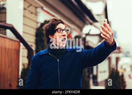 Junger Mann nimmt Selfie und Grimacing mit geöffnetem Mund Stockfoto