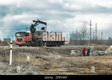 Weißrussland, Region Minsk - 11. Dezember 2019: Bauarbeiter entladen oder laden Betonringstrukturen von einem LKW oder Fahrzeug in einem Industriegebiet. Stockfoto