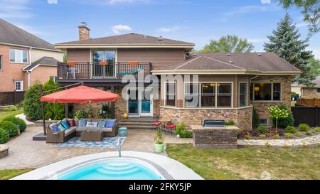 Ein wunderschöner Hinterhof mit einem im Erdgeschoss gelegenen Pool, Sitzgelegenheiten unter einem Sonnenschirm und einer betonierten Terrasse. Stockfoto