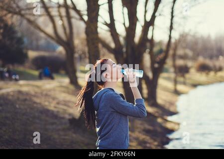 Junge Frau, die während des morgendlichen Joggens im Park Wasser trinkt Stockfoto