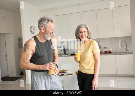 Gesundes sportlich glückliches Seniorenpaar trinkt Saft und lacht zu Hause. Stockfoto