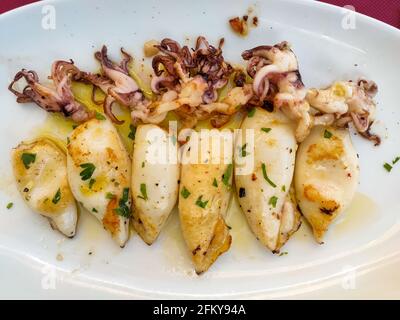 Gegrillter Tintenfisch mit Petersilie und Olivenöl-Sauce auf weißem Teller im italienischen Restaurant in venedig. Gesunde Ernährung, mediterrane Ernährung. Stockfoto