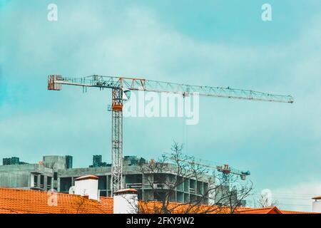 Ein Turmkran neben einem unfertigen Betongebäude auf einer Baustelle gegen einen blauen Himmel. Stockfoto