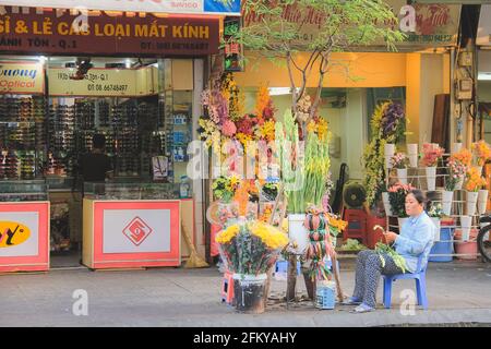 Hanoi, Vietnam - 10 2019. März: Ein lokaler vietnamesischer Straßenhändler trimmt Blütenstiele auf den Straßen von Ho Chi Minh City (Saigon). Stockfoto