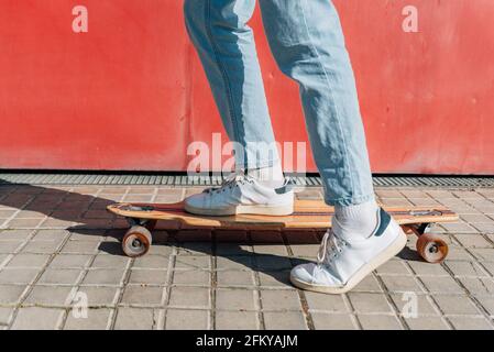 Nahaufnahme der Füße eines unverkennbaren Mannes auf einem Skateboard auf dem Straßensteig. Er projiziert einen harten Schatten auf den Boden Stockfoto