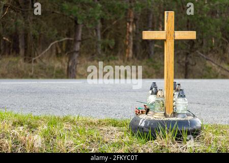 Ein Gedenkkreuz am Straßenrand mit Kerzen zum Gedenken an den tragischen Tod an einer Straße. Stockfoto