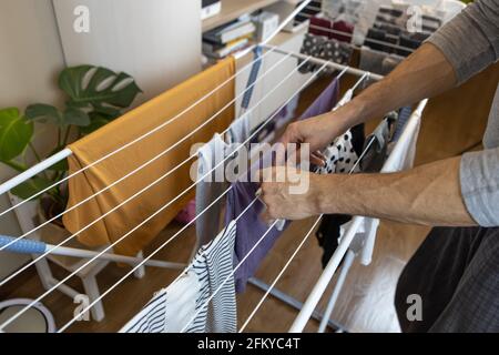 Ein Mann legt die gewaschenen Kleider auf den Trockner, der sich in einem Zimmer in der Wohnung befindet. Hygienekonzept, Männer zu Frauen im Haus zu helfen, sich zu verändern Stockfoto