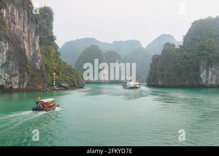 Ausflugsboote mit Touristen durchfahren das idyllische, türkisfarbene Meer und üppige, grüne tropische Kalksteinformationen in der Ha Long Bay, Vietnam. Stockfoto