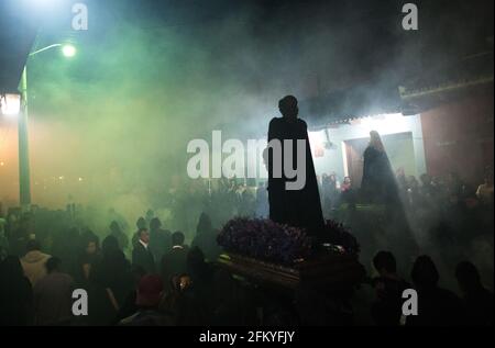 Nachts nimmt die Semana Santa-Prozession in Antigua eine geheimnisvolle, spirituelle Atmosphäre an, während Räucherrauch die Luft um eine beleuchtete Ananda füllt. Stockfoto