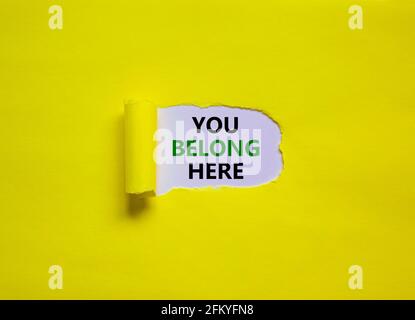 Sie gehören hier Symbol. Hinter zerrissenen gelben Papieren erscheinen die Begriffe „Du gehörst hierher“. Schöner gelber Hintergrund. Business und du gehörst hier, Stockfoto