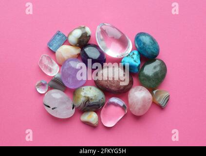 Getauchte und raue Edelsteine und Kristalle in verschiedenen Farben. Amethyst, Rosenquarz, Achat, Apatit, Aventurin, Olivin, türkis auf rosa Hintergrund. Stockfoto