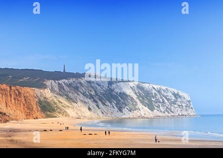 Menschen, die am Yaverland Beach unter blauem Himmel spazieren, mit Culver Down Cliff, der nördlich von Sandown Bay, Isle of Wight, England, ins Meer ragt Stockfoto