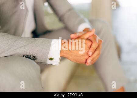 Ein Mann in einem grauen Anzug in einem weißen Hemd mit Manschettenknöpfen sitzt mit gefalteten Händen, Nahaufnahme Stockfoto