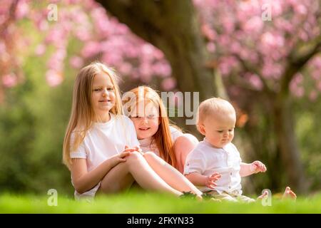 Drei kleine Kinder sitzen als Gruppe draußen Stockfoto