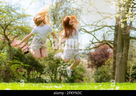 Zwei kleine Mädchen, die bei warmem Wetter fröhlich draußen springen Stockfoto