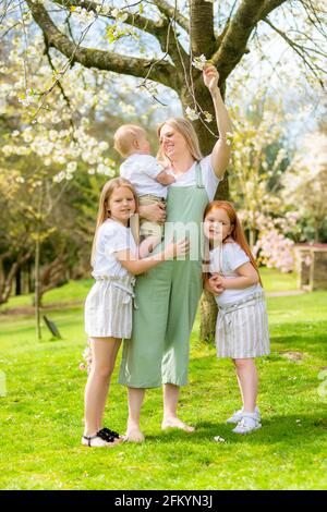 Schwangerschaftsmutter mit ihren zwei jungen Töchtern und ihrem kleinen Sohn Draußen in einem öffentlichen Park Stockfoto