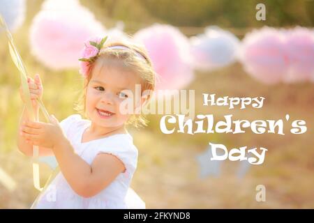 Text HAPPY CHILDREN'S DAY kleines Mädchen hält Kugeln in den Händen und lächelt. Kleines Kind auf der Party. Festliche Deko-Pompons. Stockfoto