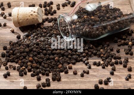 Piper nigrum - schwarze Pfefferkörner; Foto auf dunklem Holzhintergrund. Stockfoto