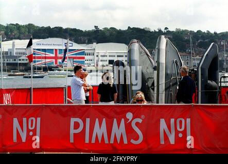 DIE LEUTE GENIESSEN EINEN NACHMITTAGSDRINK IN EINEM PRIVATEN BOOTCLUB IN WEST COWES GEGENÜBER IN EAST COWES, DER GKN WESTLANDS AEROSPACE FABRIK, DIE EINER DER HAUPTARBEITGEBER AUF DER INSEL IST, IST COWES WEEK BEI DEN ARBEITERN DORT NICHT BELIEBT. ISLE OF WIGHT Stockfoto