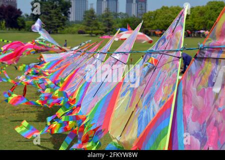 Eine Reihe von bunten Regenbogendrachen zum Verkauf in einem Park, die an einem Tag, der perfekt zum Fliegen ist, im Wind flattern. Stockfoto