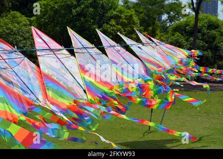 Eine Reihe von bunten Regenbogendrachen zum Verkauf in einem Park, die an einem Tag, der perfekt zum Fliegen ist, im Wind flattern. Stockfoto