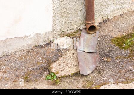 Regenwasserabfluss vom Dach. Rostiger Schlauch für Regenwasserabfluss zur Straße und Metallbleche angebracht. Ein sehr primitiver Sturmflut. Stockfoto