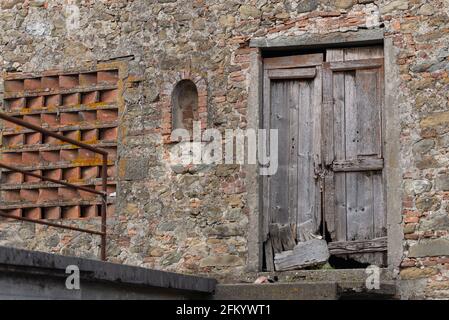 Die Mauer eines alten Steinscheals. Eine alte und verfallene Holztür in einer alten Scheune in der Toskana. Stockfoto