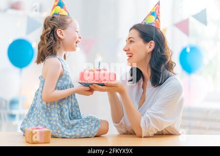 Das Kind bläst die Kerzen auf dem Kuchen aus. Mutter und Tochter feiern Geburtstag. Stockfoto