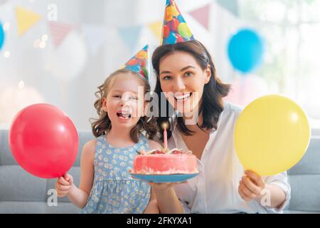 Das Kind bläst die Kerzen auf dem Kuchen aus. Mutter und Tochter feiern Geburtstag. Stockfoto