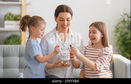 Mutter und Töchter halten Geldkasten, Mädchen setzen Münze. Geldkasten, Mädchen setzen Münze. Stockfoto