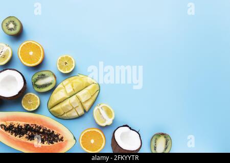 Verschiedene frische, tropische Schnittfrüchte auf blauem Hintergrund. Papaya, Orange, Banane, Kokosnuss, Mango, Kiwi und Zitrone Draufsicht flach Lay mit Kopieplatz für Stockfoto