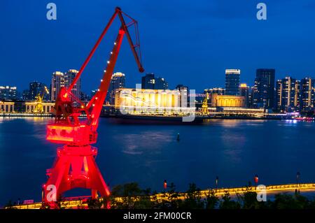 Ein alter Schiffskran im Bezirk Yanpu rahmt ein Frachtschiff und Gebäude auf der Pudong-Seite des Huangpu-Flusses, Shanghai, China. Stockfoto