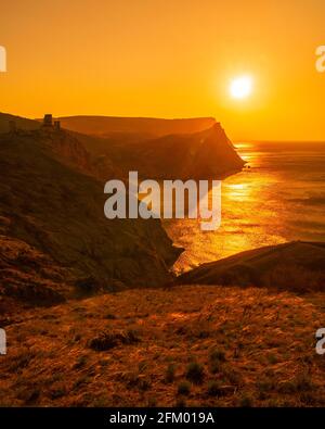 Ein rot brennender Sonnenuntergang mit dem Silhouett einer Klippe Und Burg über dem Meer Stockfoto