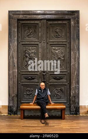 Älterer Mann sitzt auf einer Holzbank vor einer geschnitzten Holztür im Deutschen Geschichtsmuseum unter den Linden, Mitte, Berlin Stockfoto